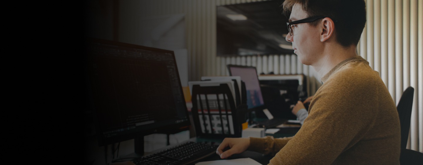 man with glasses sitting in an office on a desktop computer