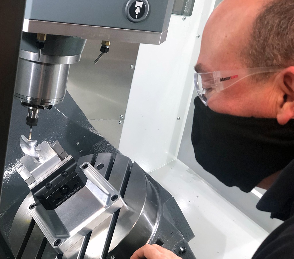 Male wearing safety goggles analyzing a silver metal 5-axis toolpath on a part