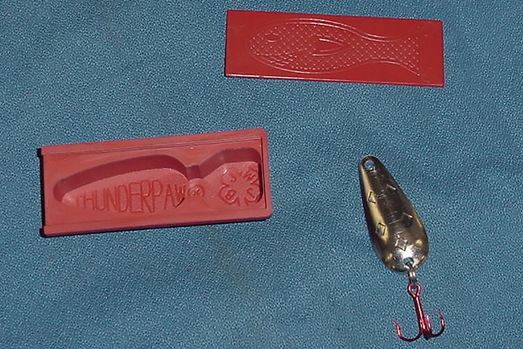 Metal fishing lure and red rubber. mold on a blue background
