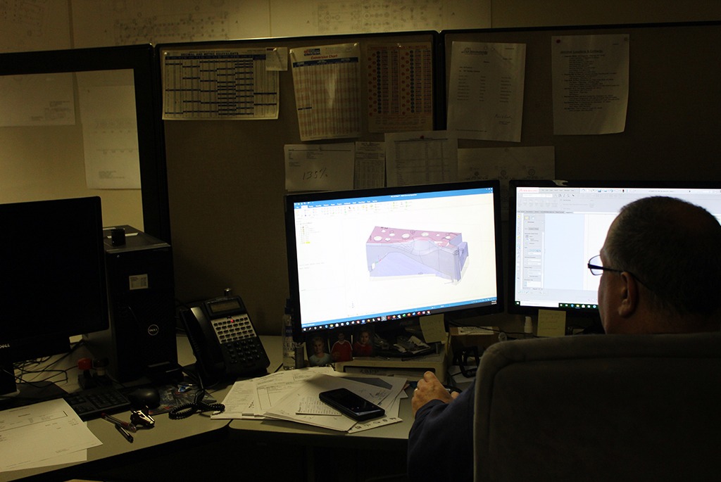 Man sitting at desk using mastercam 3D model software on double monitors