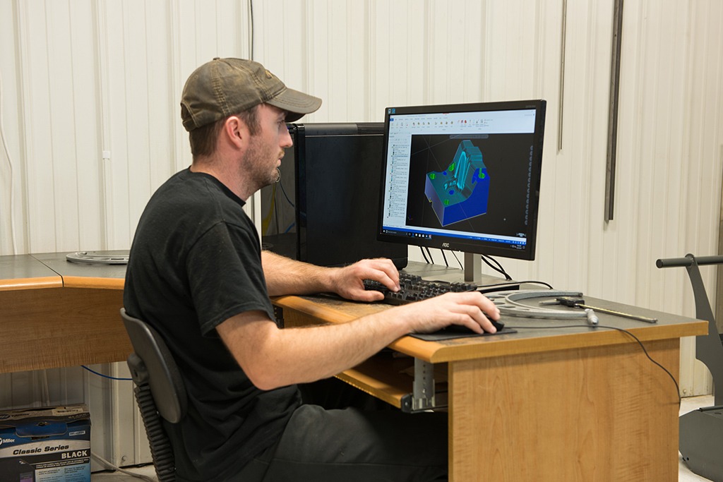 A triple C employee sitting at a desk and programming with mastercam on a monitor
