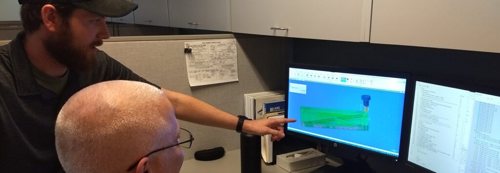 A man shows a second man sitting at a desk the royell computer program