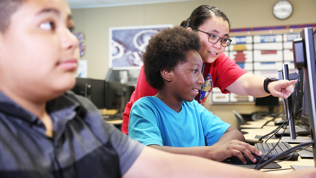 A female teacher helping a young male student at a computer