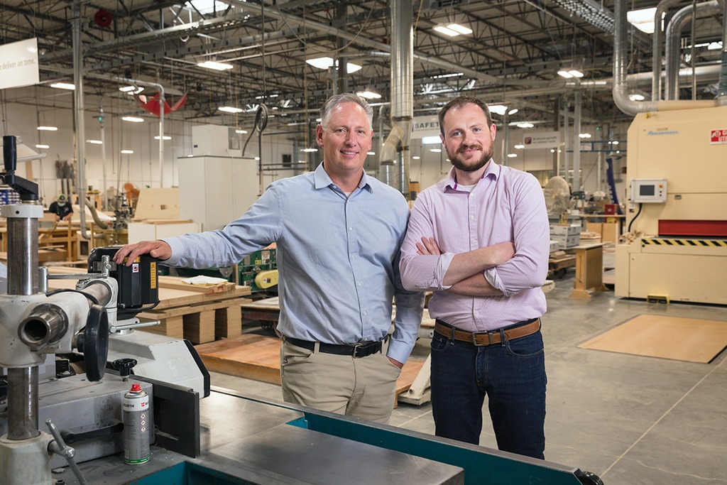 Eric Fetzer and David Musser smiling inside an industrial woodshop warehouse