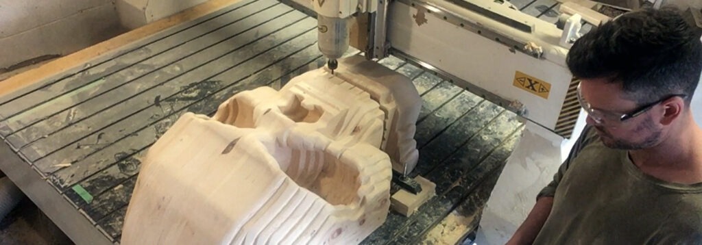 Marcel Jordan watching wood cutter machine carve a large wooden skull