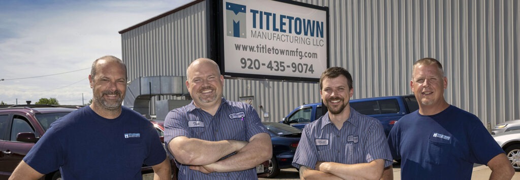 Four males smiling at the camera outside of Titletown Manufacturing LLC ware house
