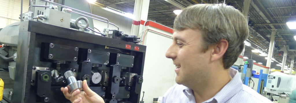 Trent Turner smiling and inserting a silver mechanical part into a machine