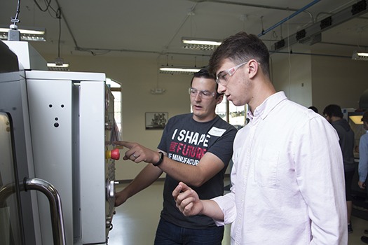 Two men wearing clear workshop glasses inside a workhouse and operating machinery