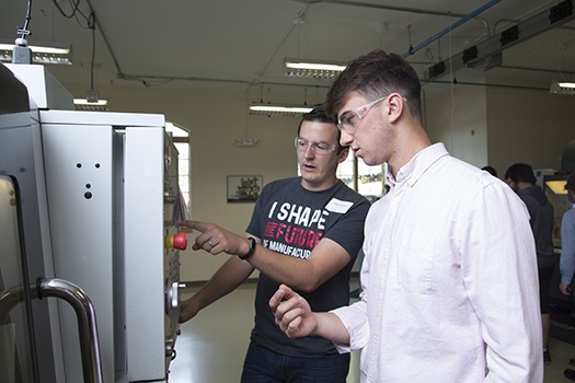 Two men wearing clear workshop glasses inside a workhouse and operating machinery 