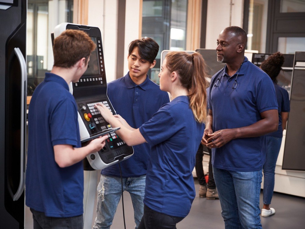 Engineer showing apprentices how to use CNC tool making machine