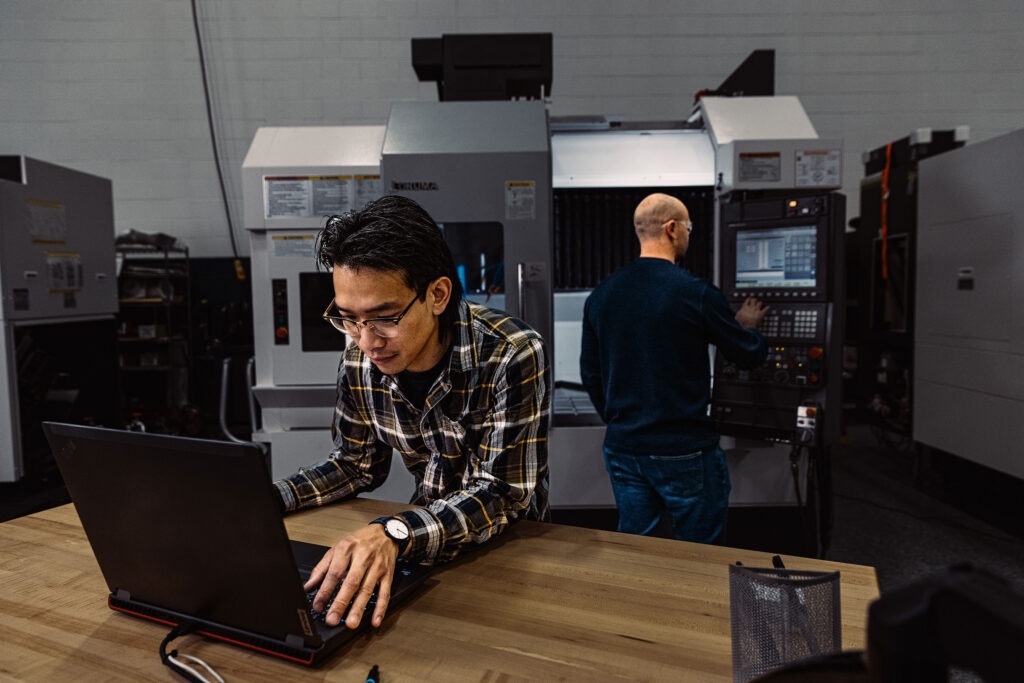 Two men at a machine shop back to back looking at screens