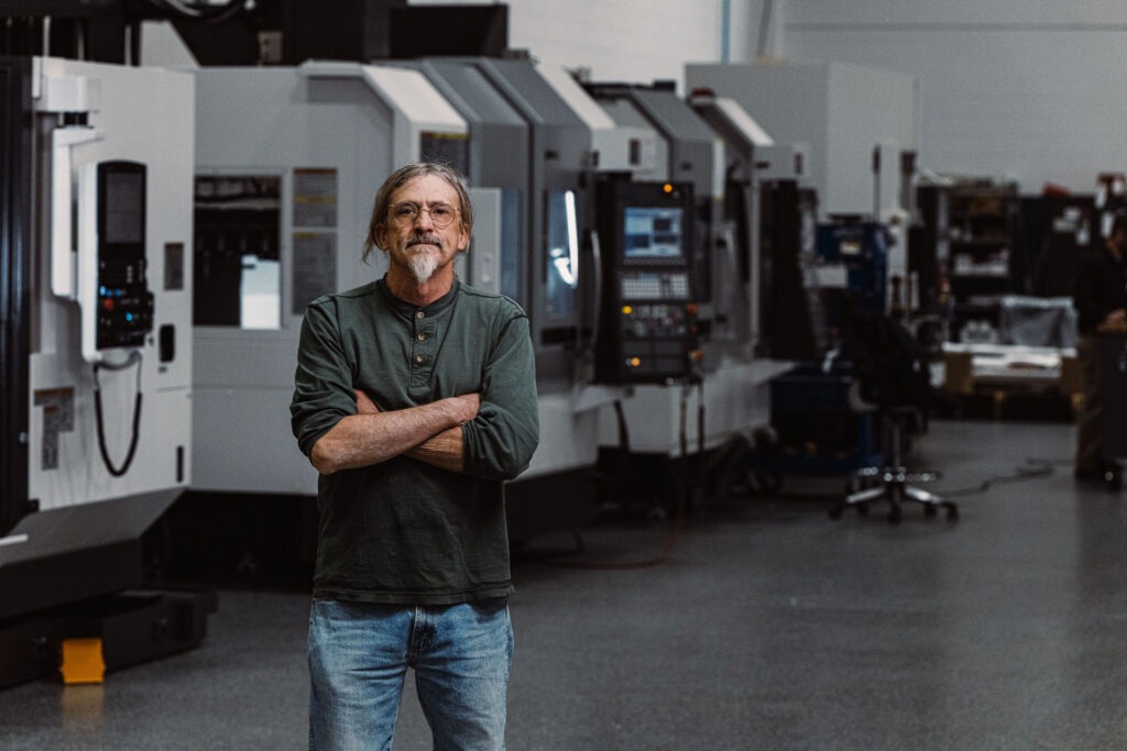 man in a machine shop standing in front of equipment with arms folded