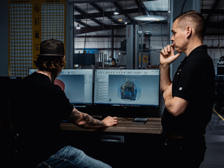 two men in a machine shop looking at screens