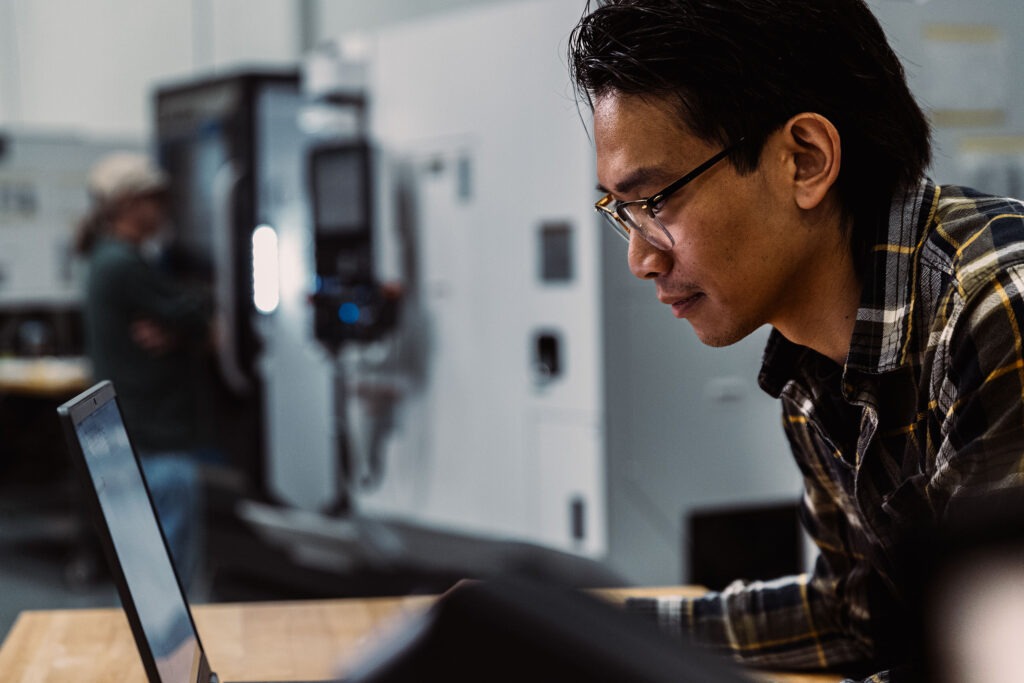 sideview of a man in a machine shop looking at a computer